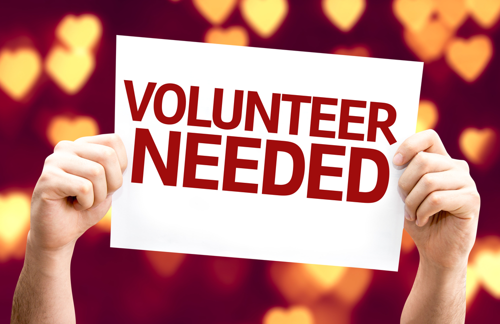 Person Holding a Volunteer Needed Card with Heart Background